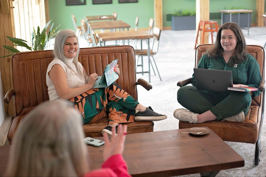 Charlotte sat on a sofa in a cafe with feet up looking relaxed and smiling Charlotte is a blonde haired female say on a sofa with her feet up, talking to her hypnotherapy students in a cafe